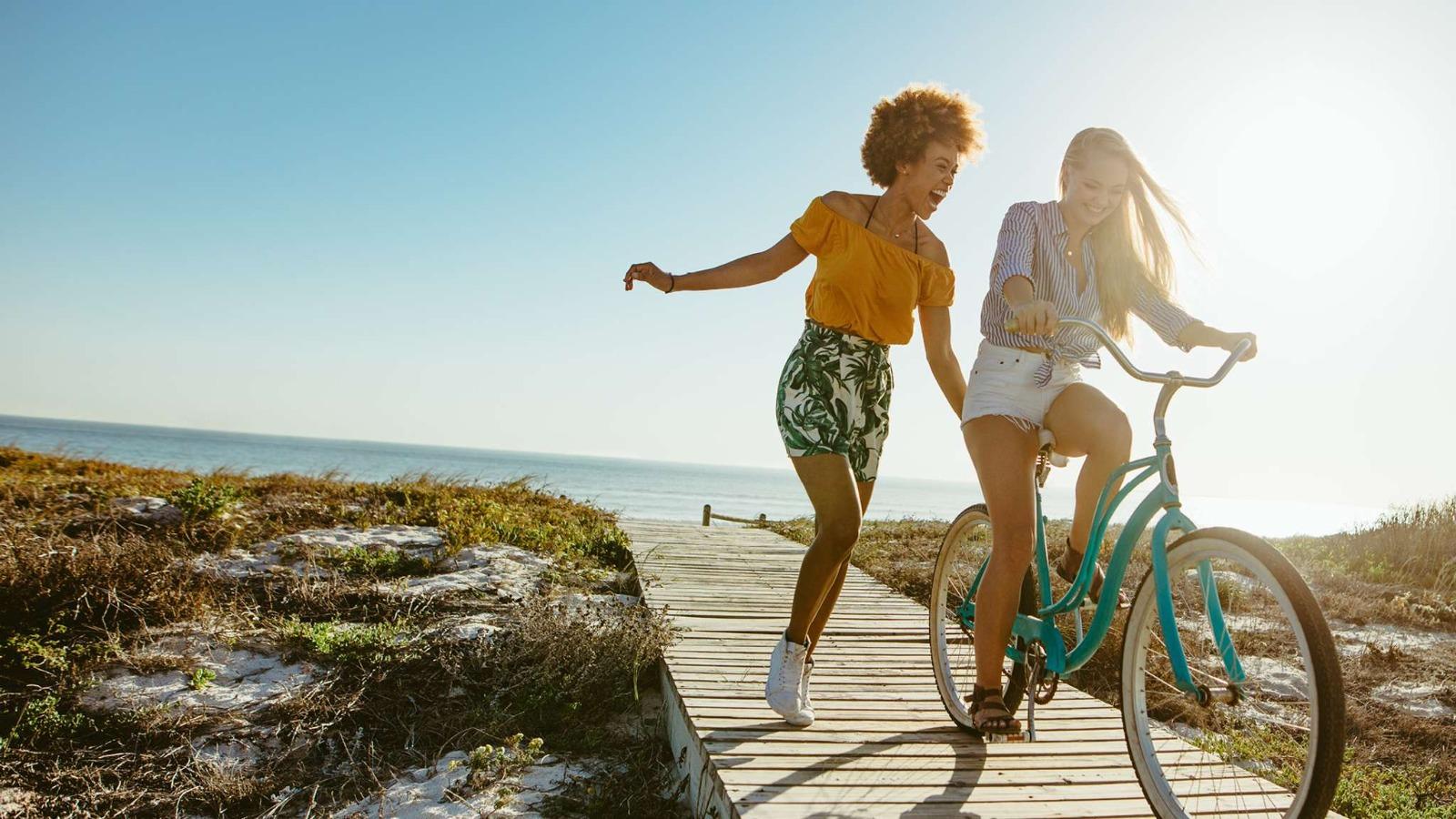 Girl riding a bike with friend by the beach
