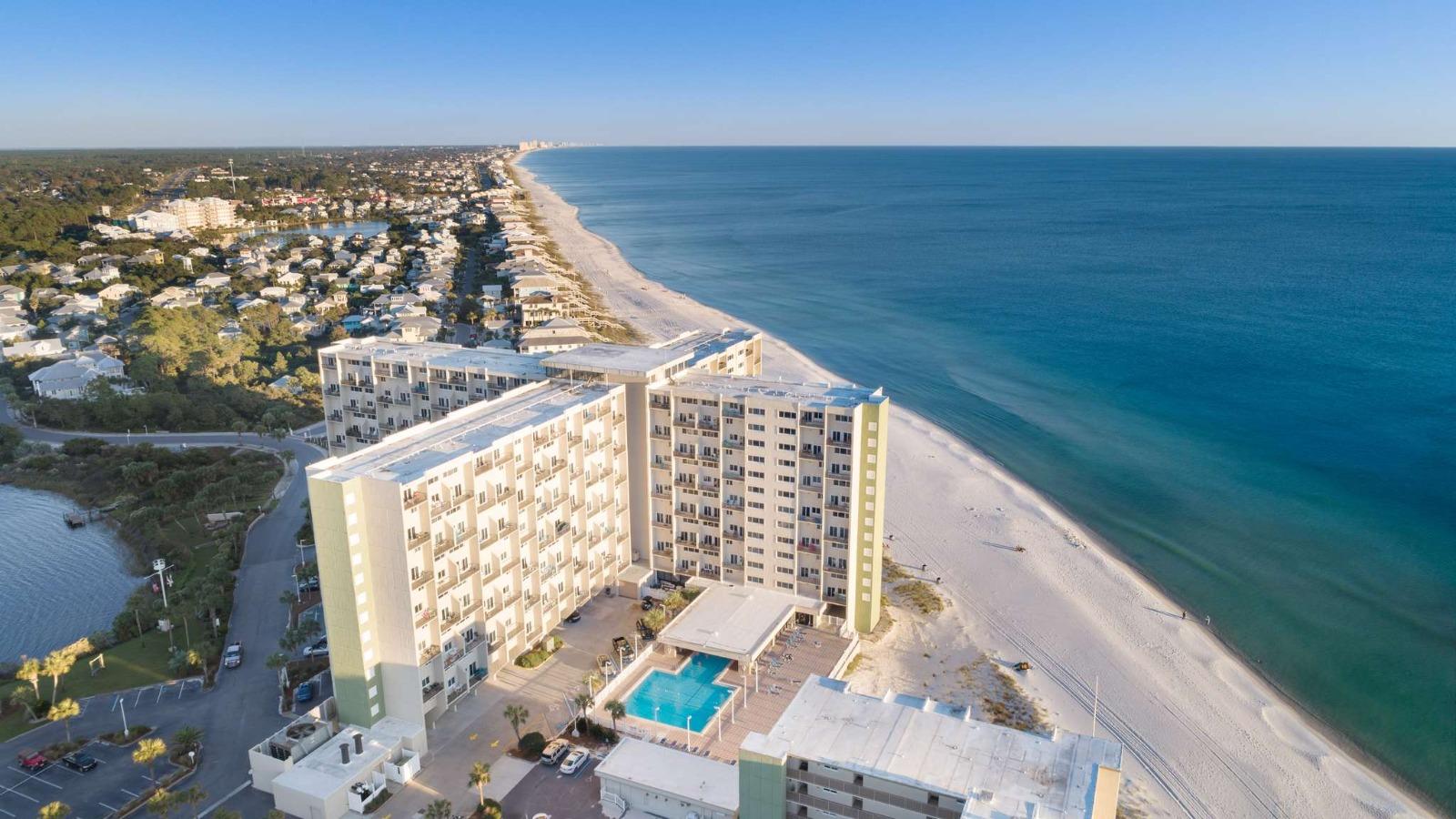 Aerial view of Pinnacle Port resort showing multi-story buildings, a pool, a white sand beach, and the ocean.