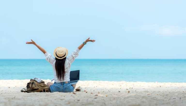 Woman sitting on the beach with laptop and arms in the air