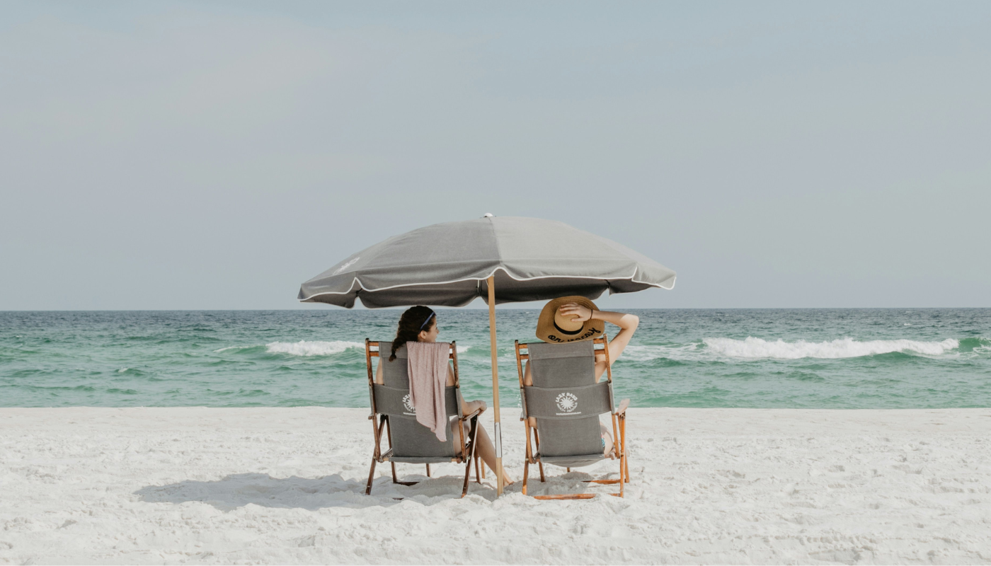 Two women under beach umbrella on the beach facing the ocean